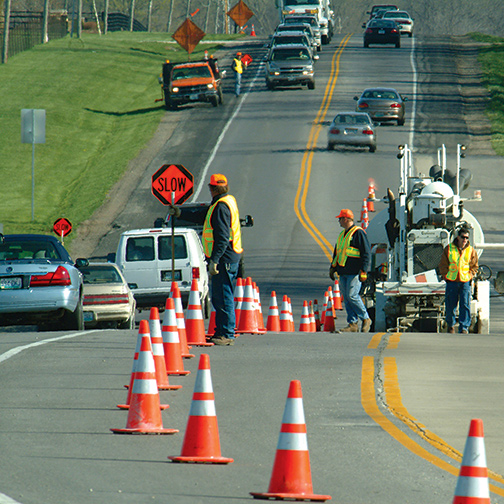 Construction on roadway with orange cones and a workers in safety gear.
